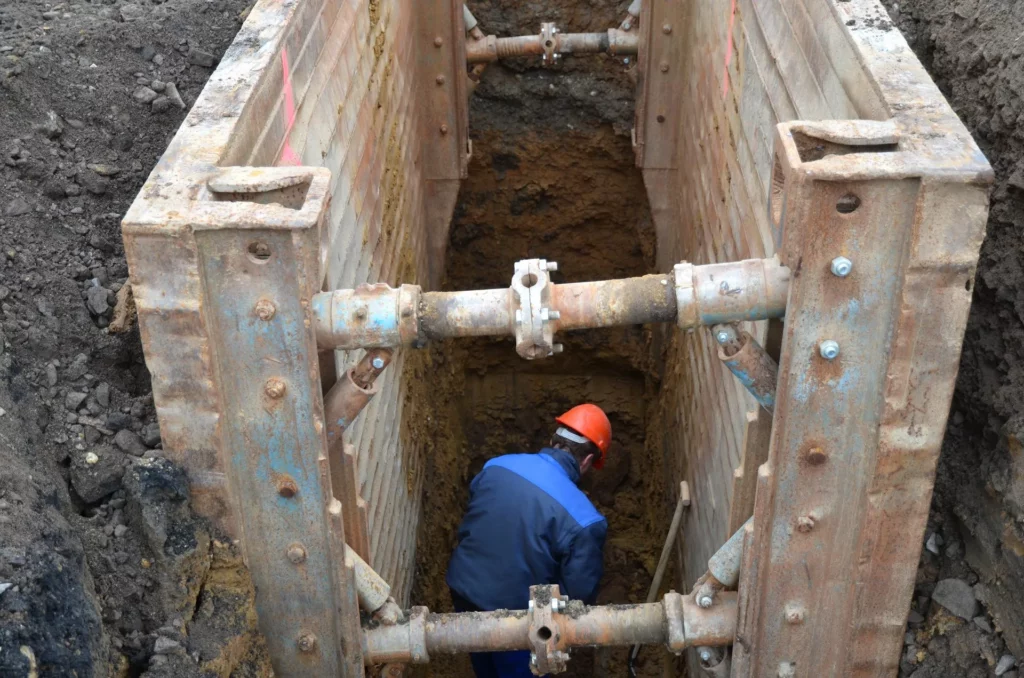 Worker performing excavation and trenching work inside a protected trench excavation system.